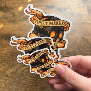 May include: Two black and orange skull stickers with the text "Without darkness there can be no light" and "Without darkness be".