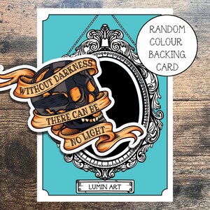 May include: A black and white skull with orange accents inside a decorative ornate frame. The skull has a banner that reads "Without darkness there can be no light". The background is turquoise blue. The text "Random Colour Backing Card" is in the top right corner. The text "LUMIN ART" is at the bottom of the image.