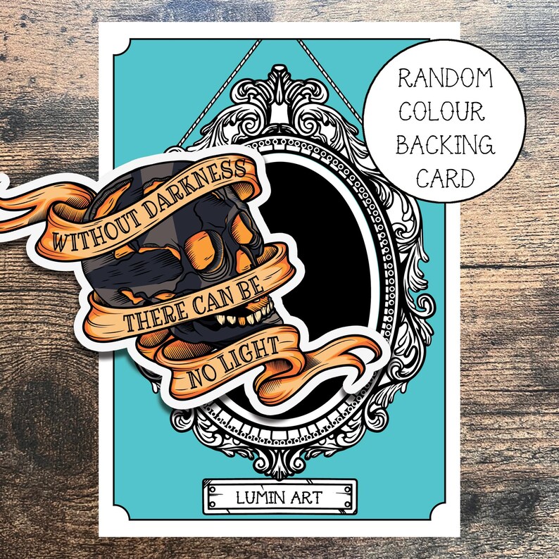 May include: A black and white skull with orange accents inside a decorative ornate frame. The skull has a banner that reads "Without darkness there can be no light". The background is turquoise blue. The text "Random Colour Backing Card" is in the top right corner. The text "LUMIN ART" is at the bottom of the image.