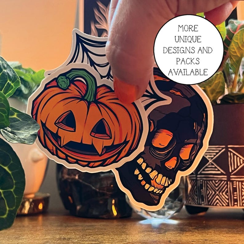 May include: Two Halloween themed stickers, one of a jack-o'-lantern with a toothy grin and the other of a skull with a toothy grin. The stickers are white with black outlines and are on a wooden surface.
