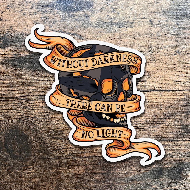 May include: A black and white skull with orange accents is surrounded by a banner with the text "Without darkness there can be no light".