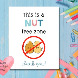 May include: A white card with the text "this is a NUT free zone" in black, teal, and pink. The card features a red circle with a line through it, containing cartoon images of an almond and a peanut. The words "thank you!" are below the image.