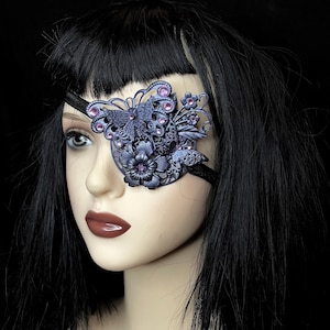 May include: A purple and black eye patch featuring a butterfly and floral design. The eye patch is embellished with rhinestones.