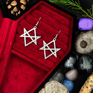 May include: A pair of silver earrings with a five-pointed star design. The earrings are displayed in a red velvet jewelry box.