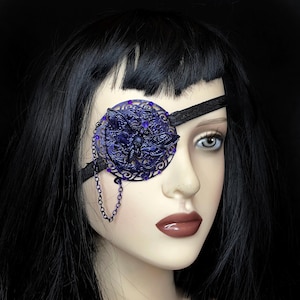 May include: A black eye patch with a purple metal filigree design and a chain. The filigree features a butterfly design with purple rhinestones.