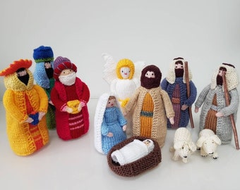 May include: Knitted nativity scene with figures of Mary, Joseph, baby Jesus, three wise men, an angel, and two sheep. The figures are all dressed in colorful robes and have detailed facial features.