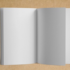 May include: A white notebook with a dotted grid pattern on the pages. The notebook is open and lying flat on a brown surface.