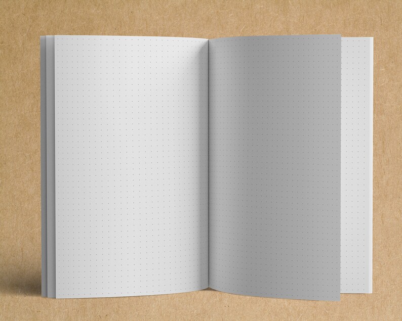 May include: A white notebook with a dotted grid pattern on the pages. The notebook is open and lying flat on a brown surface.