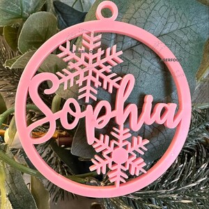 May include: Pink Christmas ornament with the name "Sophia" and snowflake designs.