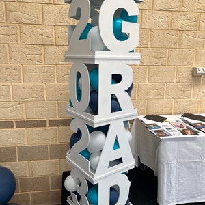 May include: White wooden block letters spelling "GRAD 2023" with blue and white balloons inside each block.