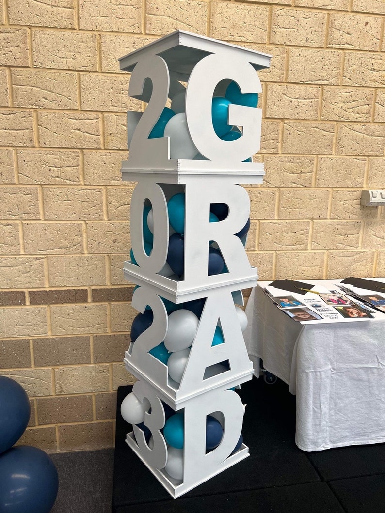 May include: White wooden block letters spelling "GRAD 2023" with blue and white balloons inside each block.