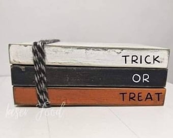 May include: A stack of three wooden signs with the words "Trick or Treat" painted in white on a black and orange background. The signs are tied together with a black and white twine.