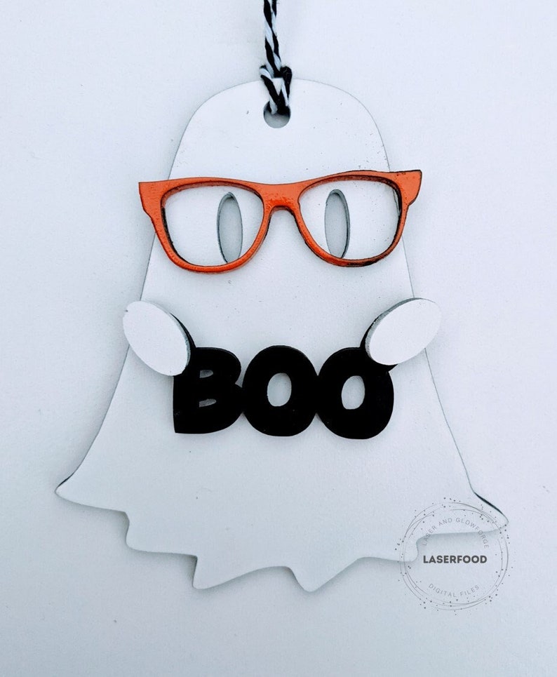 May include: White ghost cutout with orange glasses and the word "BOO" in black letters. The ghost is hanging from a black and white string.