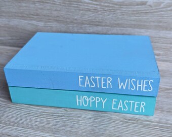 May include: Two wooden blocks stacked on top of each other. The top block is light blue and says "Easter Wishes". The bottom block is teal and says "Hoppy Easter".