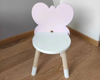 May include: A pink and white wooden butterfly chair for children. The chair has a white seat and a pink butterfly-shaped back.