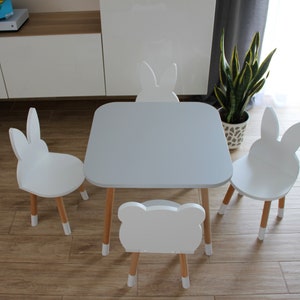 May include: A white table and four white bunny-shaped chairs with wooden legs. The table has a light gray top. The chairs are arranged around the table.