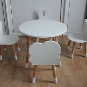 May include: A white children's table and chairs set with a cloud-shaped chair and bunny-shaped chairs. The table and chairs have wooden legs.