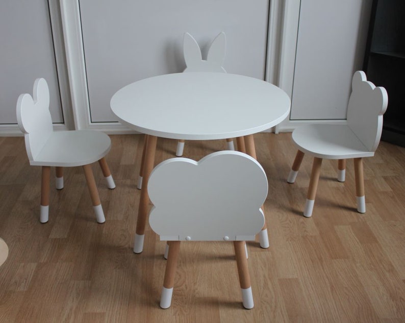 May include: A white children's table and chairs set with a cloud-shaped chair and bunny-shaped chairs. The table and chairs have wooden legs.