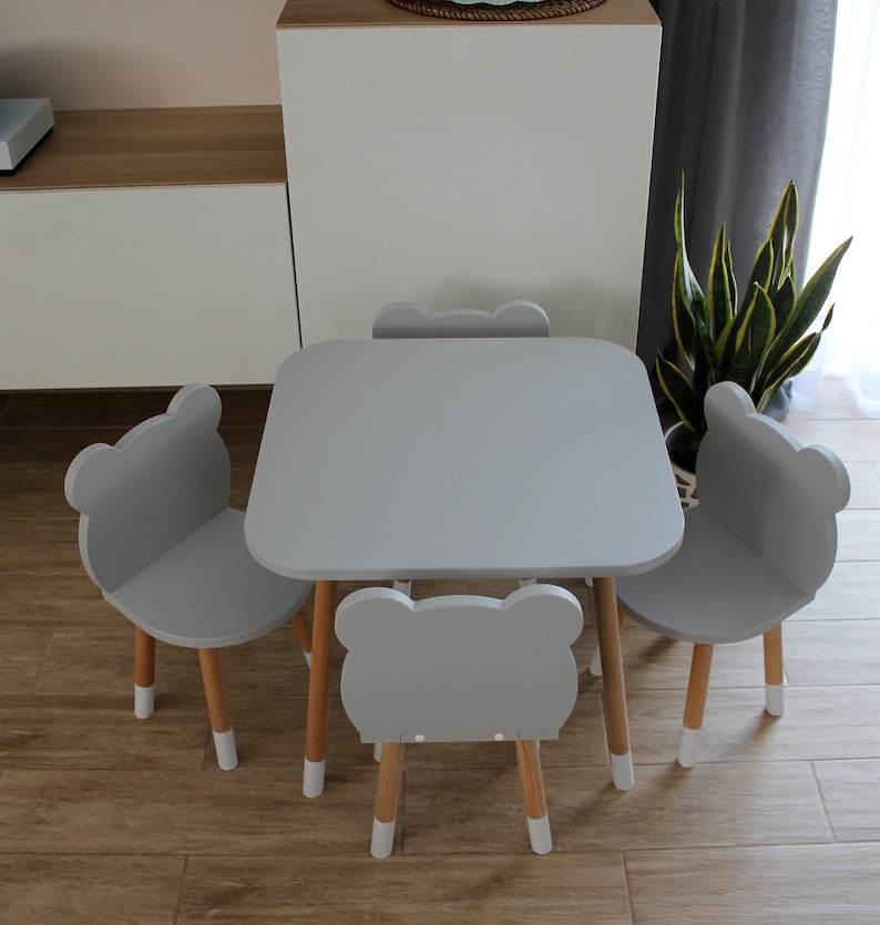 May include: A gray children's table and four chairs with bear-shaped backs. The table and chairs have a light gray finish and wooden legs.