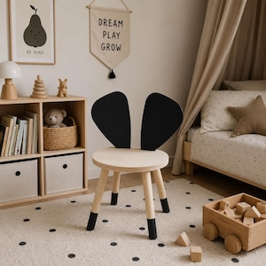 Op de afbeelding: Houten kinderstoel met een ronde zitting en een zwarte rugleuning in de vorm van konijnenoren. De stoel heeft vier poten met zwarte uiteinden. De kamer heeft ook een houten speelgoedwagen, een ingelijste perenprint en een banner met 'DREAM PLAY GROW'.