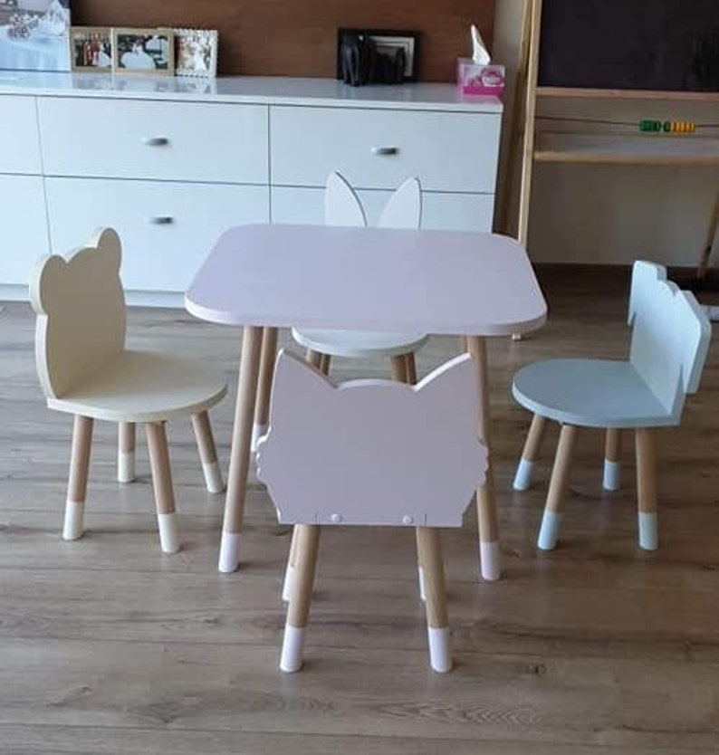 May include: A pink children's table and four chairs. The chairs are shaped like animals, including a cat, a bunny, and two bears. The table and chairs are made of wood and have a white paint finish.