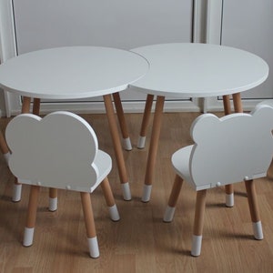 May include: A white children's table and four chairs. The table is round and has a white top and wooden legs. The chairs are all different shapes, with animal-shaped backs. The chairs have white tops and wooden legs.