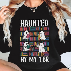 May include: Black sweatshirt with a graphic of ghosts reading books on a bookshelf. The text "Haunted by my TBR" is printed below the graphic.