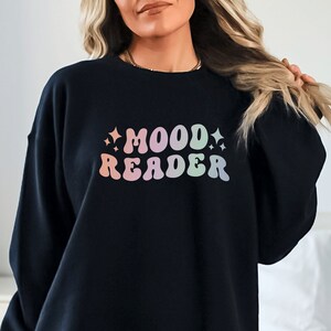 Könnte beinhalten: Schwarzer Pullover mit einem regenbogenfarbenen Aufdruck, der in einer Retro-Schrift "MOOD READER" lautet.