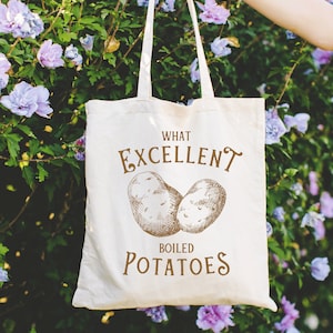 Puede incluir: Una bolsa de tela blanca con el texto "What Excellent Boiled Potatoes" impreso en marrón. Dos patatas marrones están ilustradas en la bolsa.