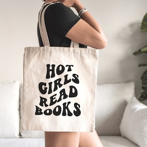K&ouml;nnte beinhalten: Eine wei&szlig;e Canvas-Tragetasche mit schwarzem Text, der in einer Retro-Schrift "HOT GIRLS READ BOOKS" lautet.