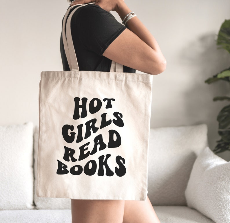K&ouml;nnte beinhalten: Eine wei&szlig;e Canvas-Tragetasche mit schwarzem Text, der in einer Retro-Schrift "HOT GIRLS READ BOOKS" lautet.