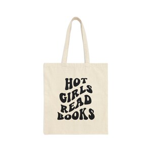 K&ouml;nnte beinhalten: Eine beige Tragetasche mit schwarzem Text, der in einer Retro-Schrift "HOT GIRLS READ BOOKS" lautet.