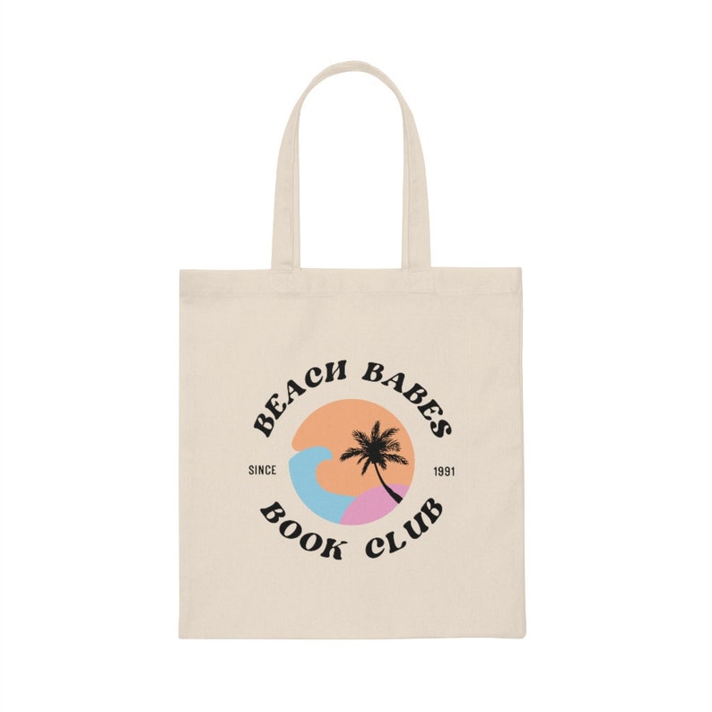 以下が含まれることがあります： ベージュのトートバッグに、黒い円のロゴがあり、「Beach Babes Book Club」と書いてあり、円の中にヤシの木と波があります。「Since 1991」という文字が円のすぐ下にあります。