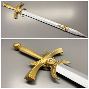 K&ouml;nnte beinhalten: Ein Schwert mit einem metallisch goldenen Griff, geschwungenen Parierstangendetails und einem kreisf&ouml;rmigen Emblem. Die Klinge ist silberfarben mit einer spitzen Klinge und einem goldenen rautenf&ouml;rmigen Akzentst&uuml;ck entlang der Klinge.