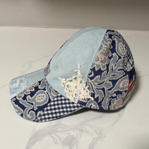 May include: A patchwork baseball cap with a light blue denim crown, paisley and gingham patterned panels, and a decorative white lace accent. The brim has a distressed, frayed edge.