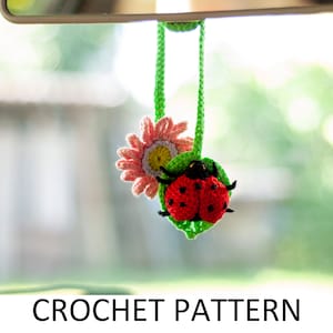 Puede incluir: Patrón de crochet para un amuleto de coche de mariquita y flor. La mariquita es roja con manchas negras y está sentada en una hoja verde. La flor es rosa con un centro amarillo.