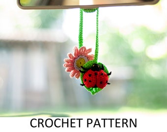Może przedstawiać: Wzór na szydełku na zawieszkę do samochodu w kształcie biedronki i kwiatu. Biedronka jest czerwona z czarnymi kropkami i siedzi na zielonym liściu. Kwiat jest różowy z żółtym środkiem.