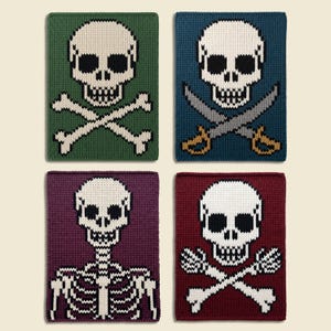 Könnte beinhalten: Vier rechteckige Strickpaneele mit Totenkopf-, Knochen- oder Skelettmotiven. Oben links ist grün, oben rechts blau mit Schwertern, unten links violett mit einem Skelett und unten rechts dunkelrot mit weißen Knochen dargestellt.