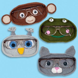 May include: Four crocheted eyeglass holders shaped like an owl, monkey, frog, and cat. Each holder has a pair of glasses resting on it.