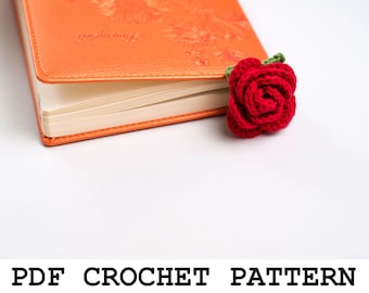 May include: A red crocheted rose bookmark with green leaves, resting on top of an orange book with the word "Journeys" embossed on the cover.