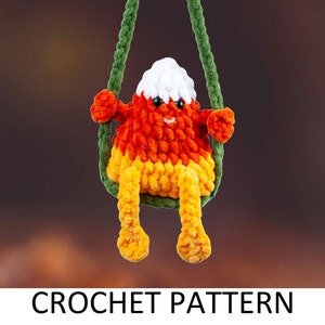 May include: A crocheted candy corn character with a white, orange, and yellow body, sitting on a green rope swing. The character has a smiling face and is wearing a green rope swing.
