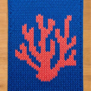 May include: A square, knitted textile in a vibrant blue color. The design features a coral-like pattern in a contrasting coral-red hue. The edges are neatly finished, creating a clean, modern look.