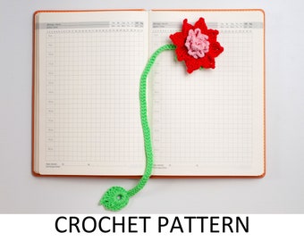 Puede incluir: Un marcapáginas de ganchillo con una flor roja y un tallo verde. El marcapáginas está unido a una agenda o un cuaderno.