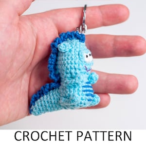 May include: A blue and white crocheted seahorse keychain with a smiling face. The keychain is held in a hand.