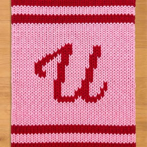 Pode incluir: Um quadrado de malha em tons de vermelho e rosa. A borda e a letra "W" são vermelhas, enquanto o fundo e as listras são rosa. O "W" está centralizado no quadrado.