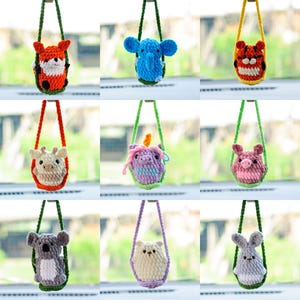May include: Nine crocheted animal plushies hanging from green strings. The plushies are a fox, elephant, tiger, giraffe, unicorn, pig, koala, bear, and rabbit. Each plushie is in a different colour and has a different expression.