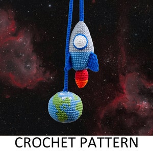 May include: Crochet pattern for a blue and gray rocket with a red flame and a green and blue earth hanging from a string against a black background with red nebulae.