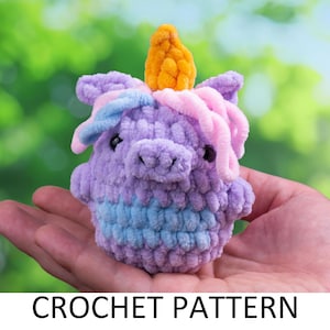 May include: A crocheted unicorn toy with a purple body, blue and pink mane, and a yellow horn. The toy is being held in a person's hand.