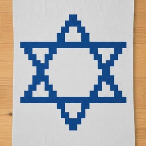 May include: White rectangular towel featuring a blue Star of David design. The star is composed of pixelated blocks, creating a geometric pattern. The towel is likely made of a soft, absorbent material, suitable for use in a bathroom or kitchen.