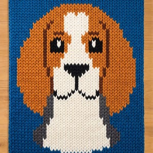 Könnte beinhalten: Ein gestricktes Quadrat mit einem Beagle-Hund-Design. Der Kopf des Hundes ist in Braun-, Weiß-, Schwarz- und Grautönen gehalten, vor einem leuchtend blauen Hintergrund. Das Stück weist eine sichtbare Strickstruktur auf.